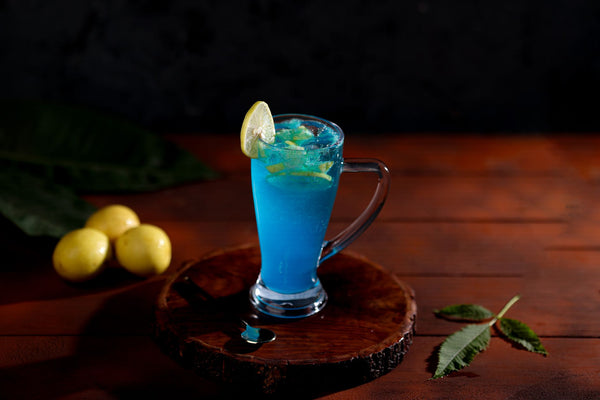 Chilled blue lemonade in a glass mug with mint and lemon slice on a wooden table.