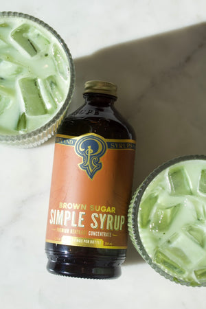 A bottle of Brown Sugar Simple sandwiched between two iced matchas.
