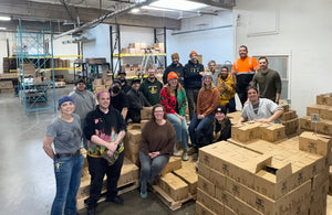 The Portland Syrups team posing together in our warehouse surrounded by stacks of cardboard boxes on pallets.